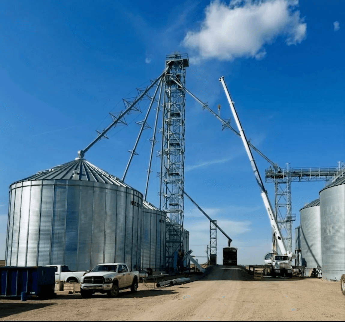 Bucket elevator tower with spouting feeding a new grain bin, service truck in the foreground