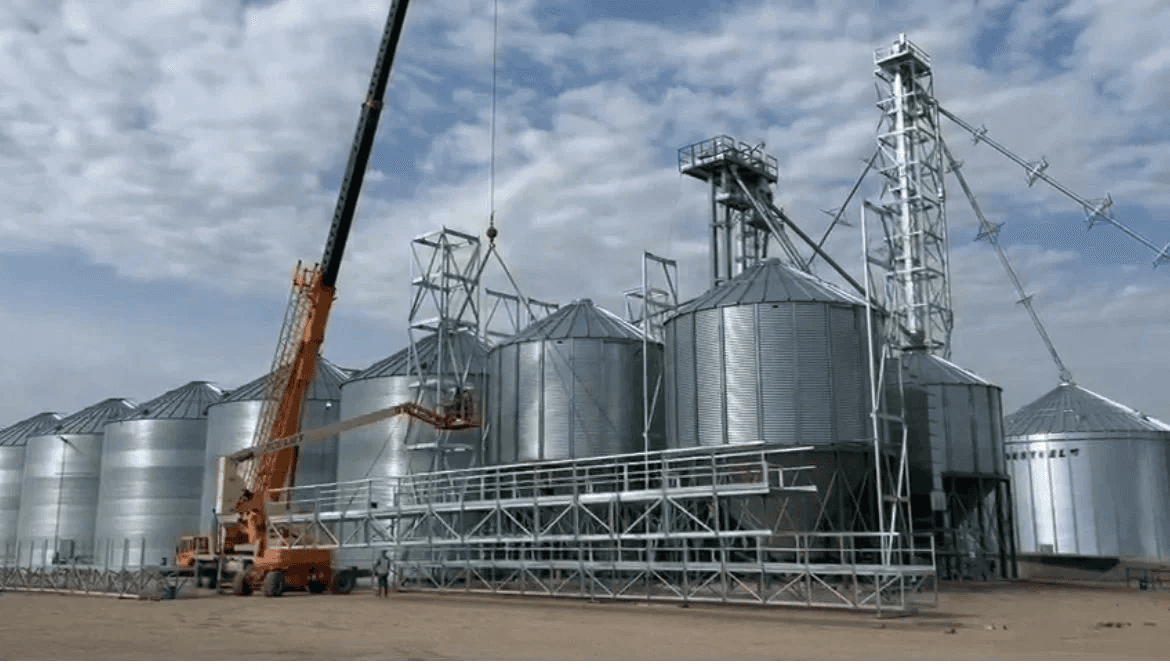 Crane and manlift installing catwalk truss between grain bins on a new yard