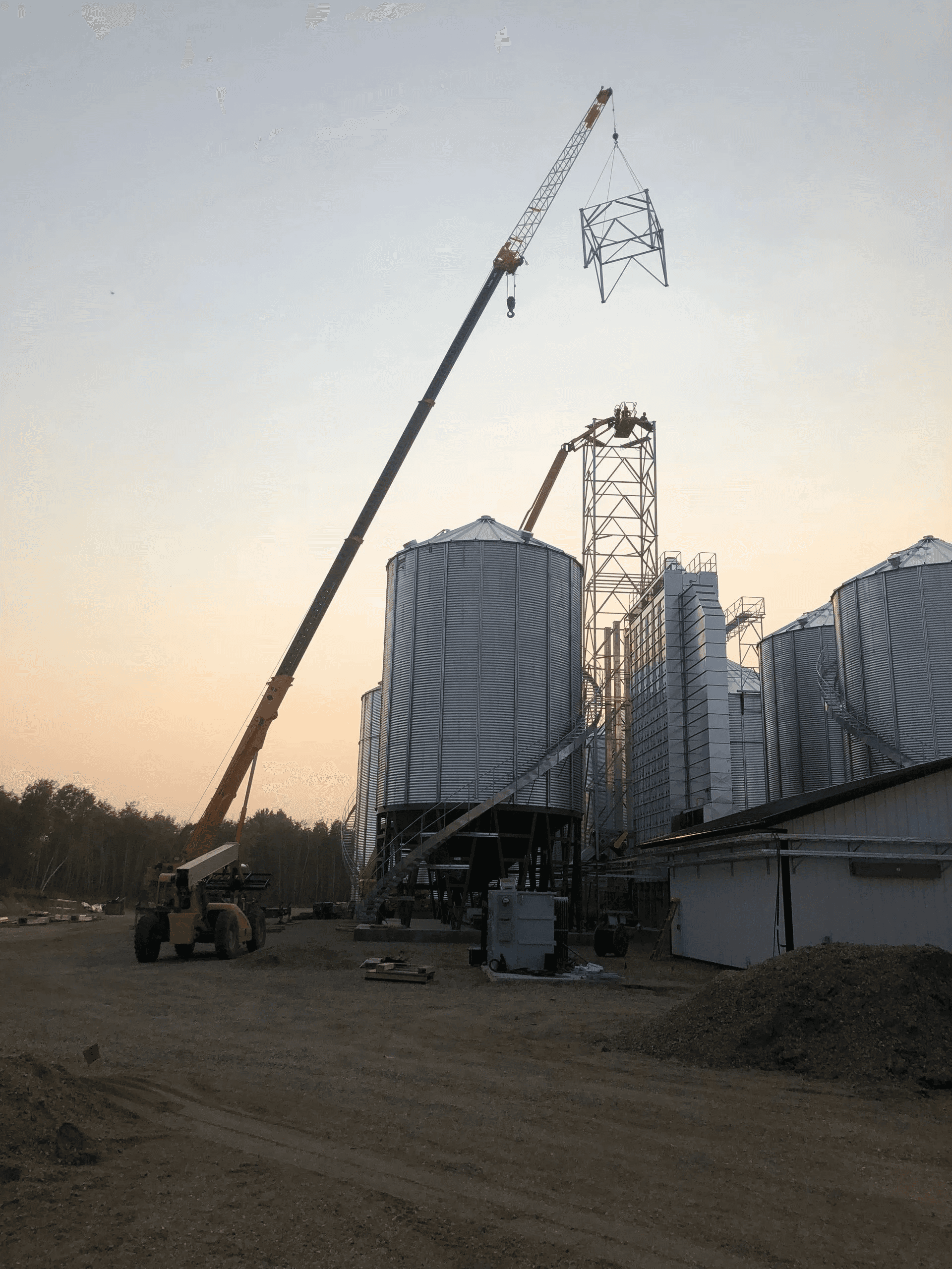 Crane lifting a tower section onto a bucket elevator tower at dusk