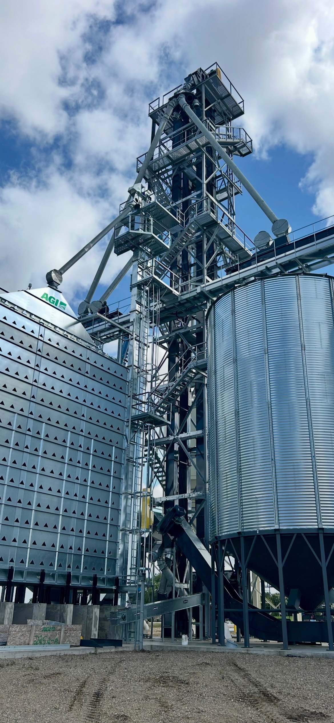 Galvanized RapiTower bucket elevator support tower with stairs and spouting between a grain dryer and a hopper bin
