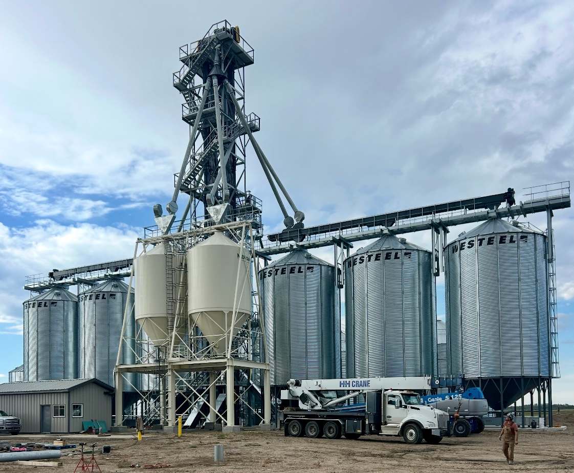 RapiTower with wrap-around stairs and spouting over hopper tanks and a row of grain bins, crane truck in front